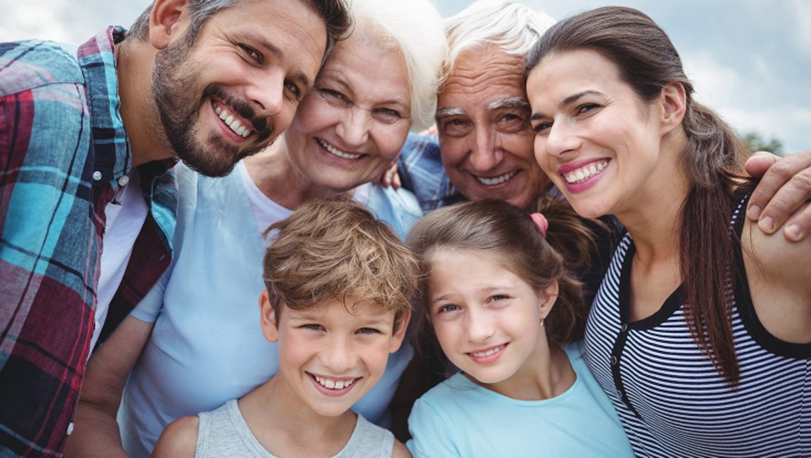 Sechs Mitglieder einer mehrgenerationen Familie posieren nah beieinander und lächeln in die Kamera